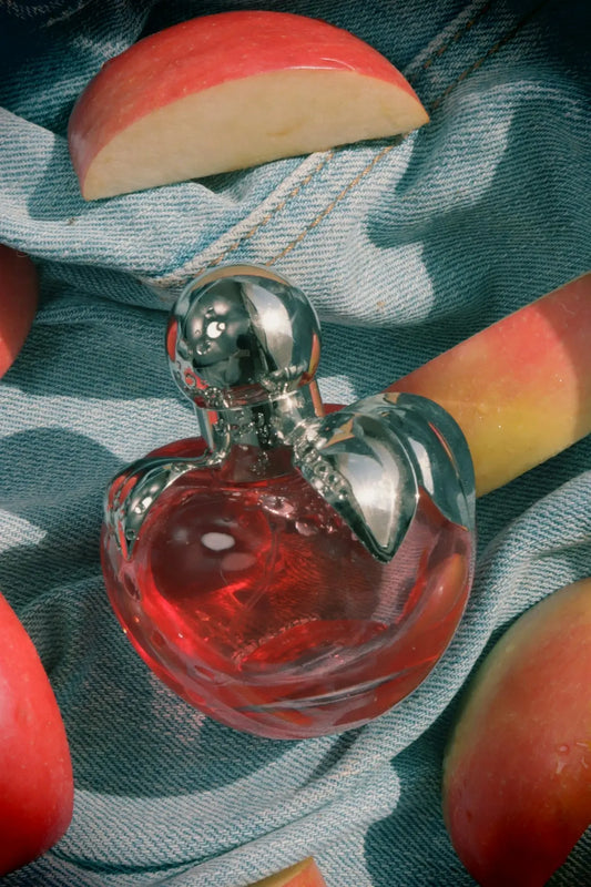 Perfume bottle and apple slices on denim fabric.