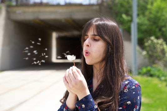 a woman blowing a dandelion with her hands