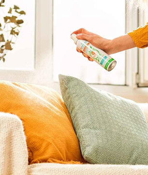 Utilisation du spray Puressentiel sur un coussin dans un salon, pour désinfecter et parfumer les textiles. Parfait pour l'entretien quotidien de la maison.