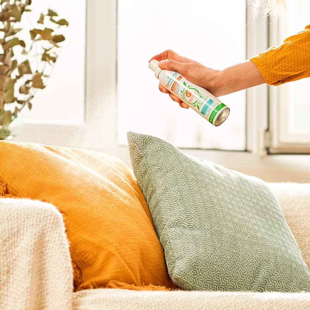 Utilisation du spray Puressentiel sur un coussin dans un salon, pour désinfecter et parfumer les textiles. Parfait pour l'entretien quotidien de la maison.